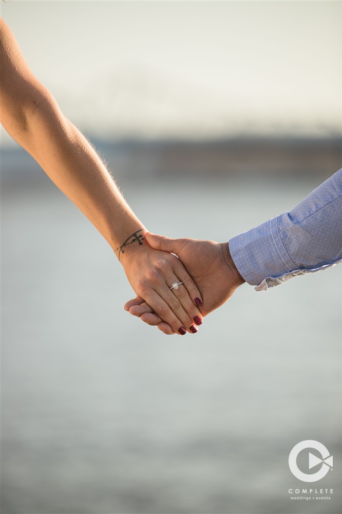 engagement ring pic of couple holdingg hand by lake