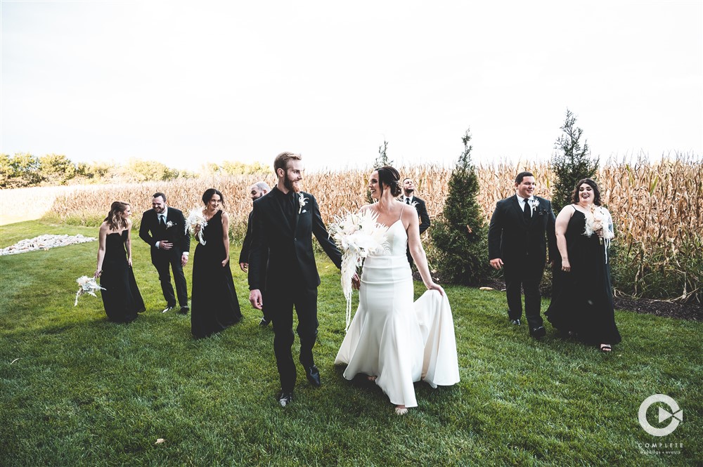 Breanna + Alex wedding party walks in field wearing black and white