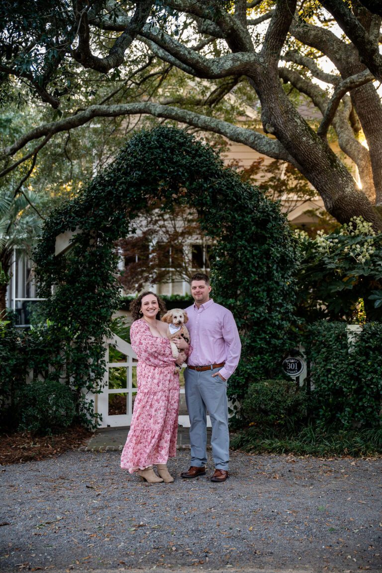Couple posing beneath a romantic ivy-covered arch during an engagement session in Charleston, South Carolina. Timeless Lowcountry engagement photography surrounded by historic oak trees and natural greenery.