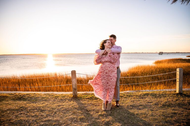 Couple sharing a romantic engagement session at sunset in Mount Pleasant, South Carolina, overlooking the marsh and waterfront. Warm golden hour engagement photography with beautiful Lowcountry scenery.