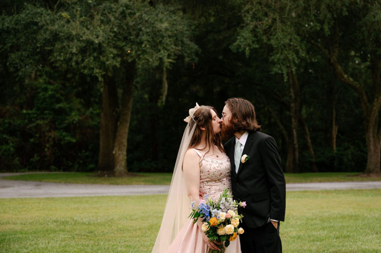 Bride and groom sharing a romantic outdoor wedding kiss surrounded by natural greenery and soft evening light. Elegant Charleston wedding photography with timeless and intimate style.