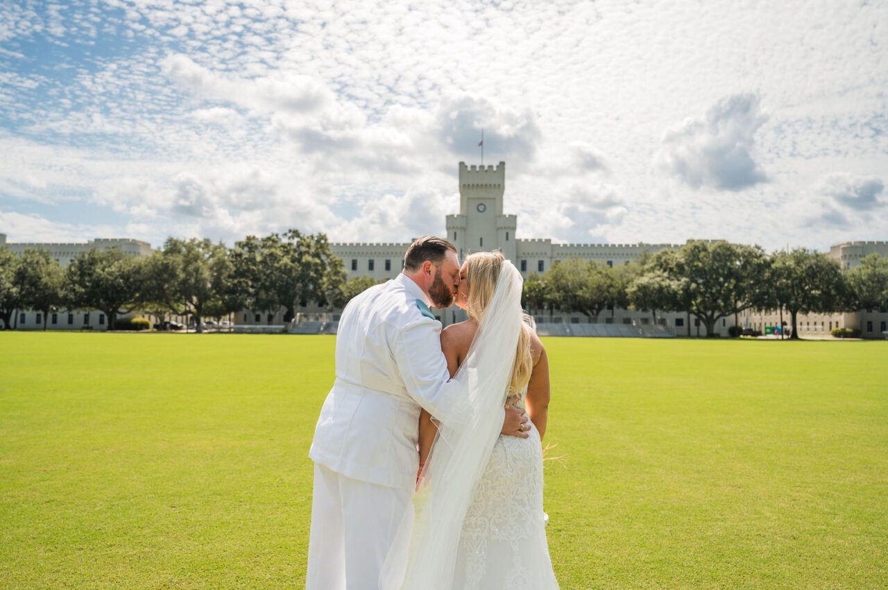Bride and groom sharing a joyful wedding portrait at The Citadel in Charleston, South Carolina, with historic white chapel architecture and bright blue skies. Romantic Charleston wedding photography with timeless and elegant style.