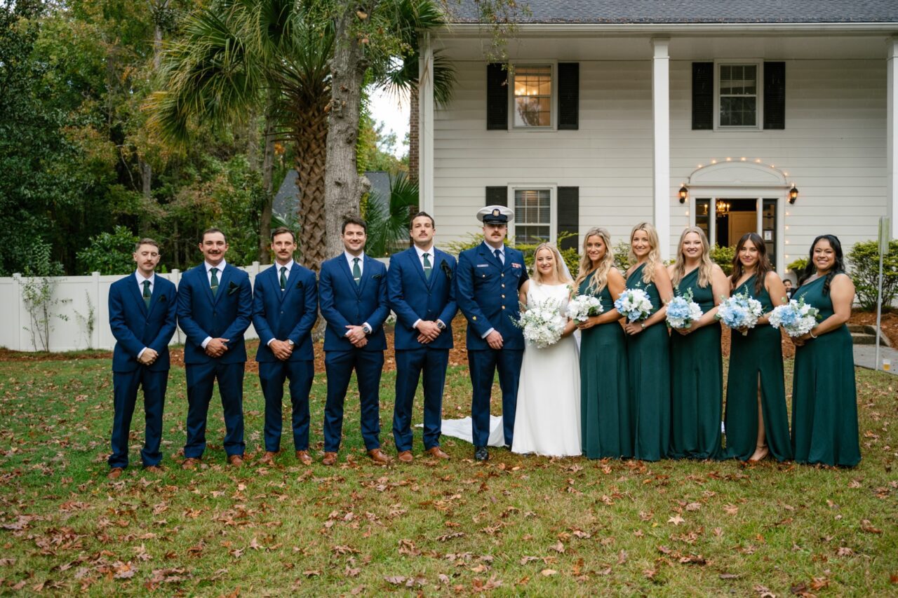 Wedding party gathered on a lawn in front of a white-sided house