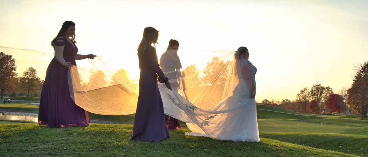 Sunset at a great Cincinnati wedding venue with the Bride walking in front of the Bridesmaids as they carry her vail.