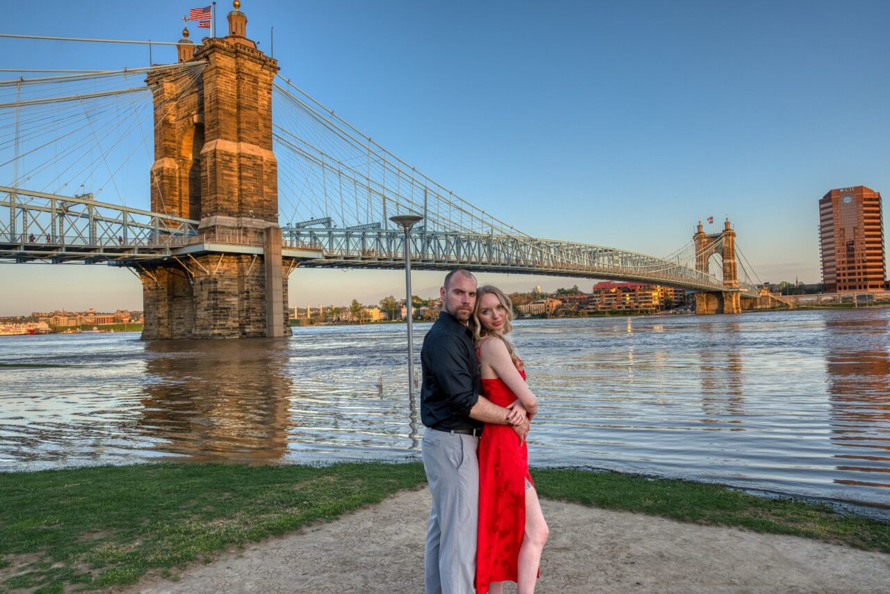 Engagement shoot in downtown Cincinnati on the river's edge. The couple ebrace looking into the camera with the Roebling Bridge in the background.
