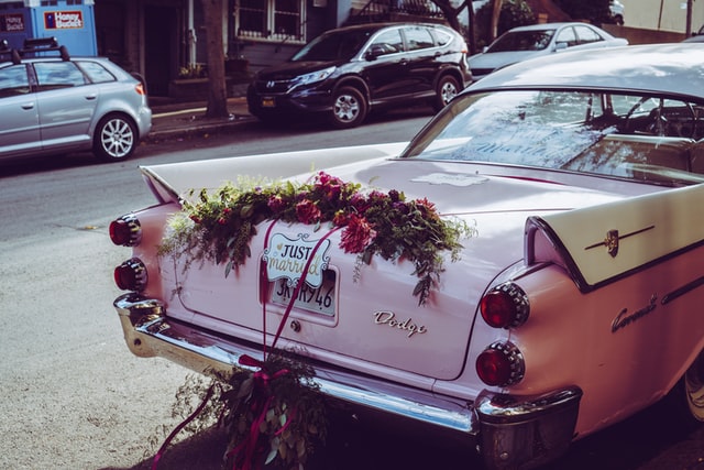 Car with wedding ornaments and a just married sign on the back.