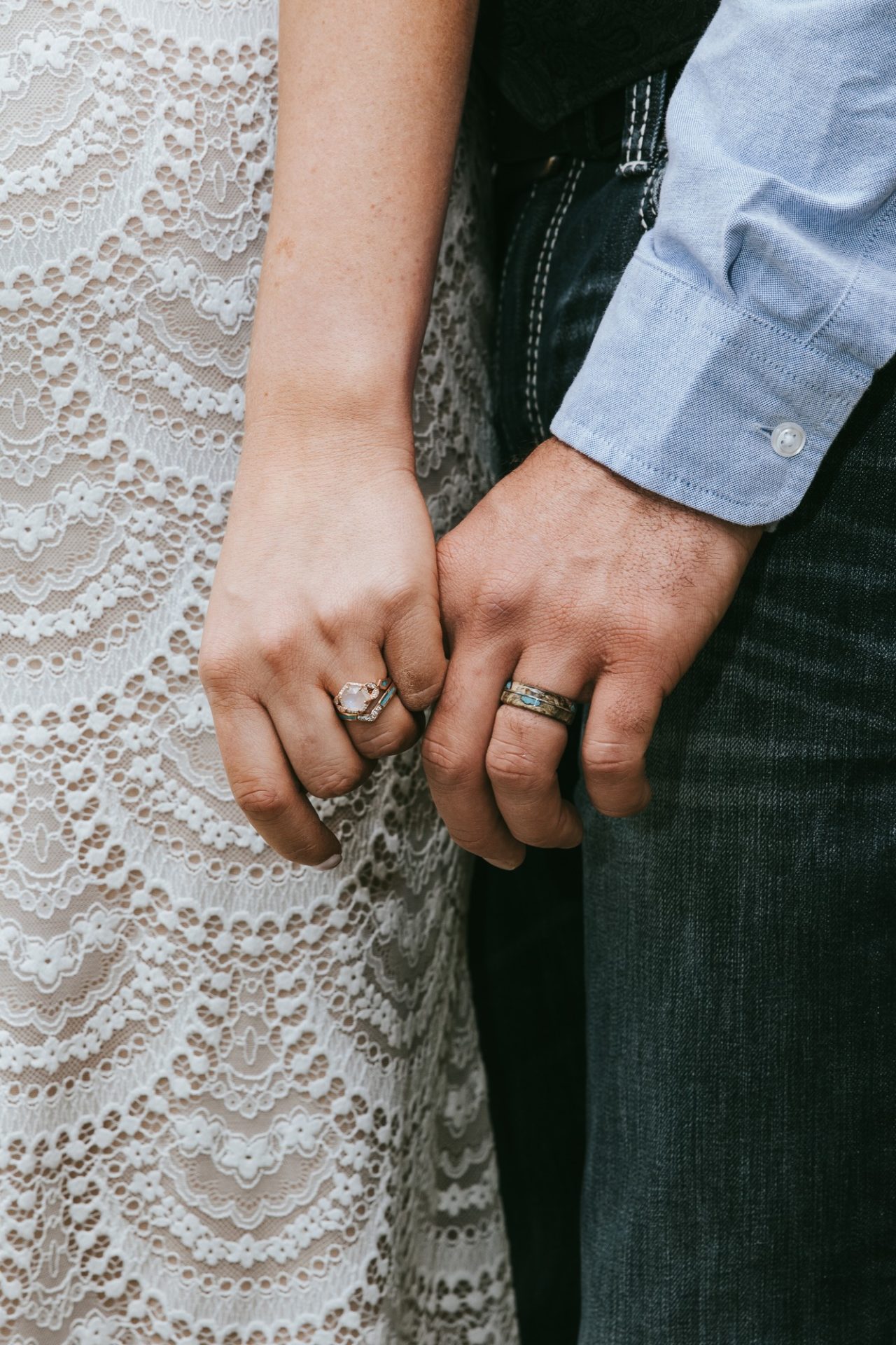 A close up picture of a bride and groom holding hands, showing off their sparkling wedding rings