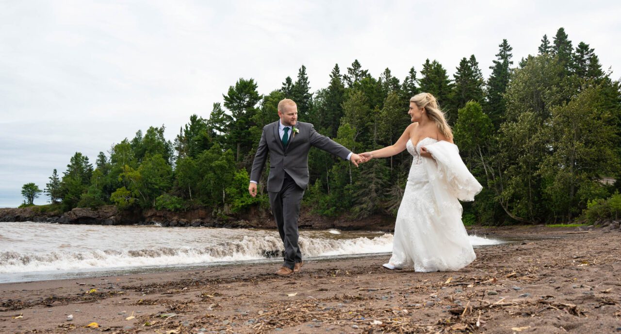 Bride and groom walking along Lake Superior shoreline at Black Beach in Silver Bay, MN