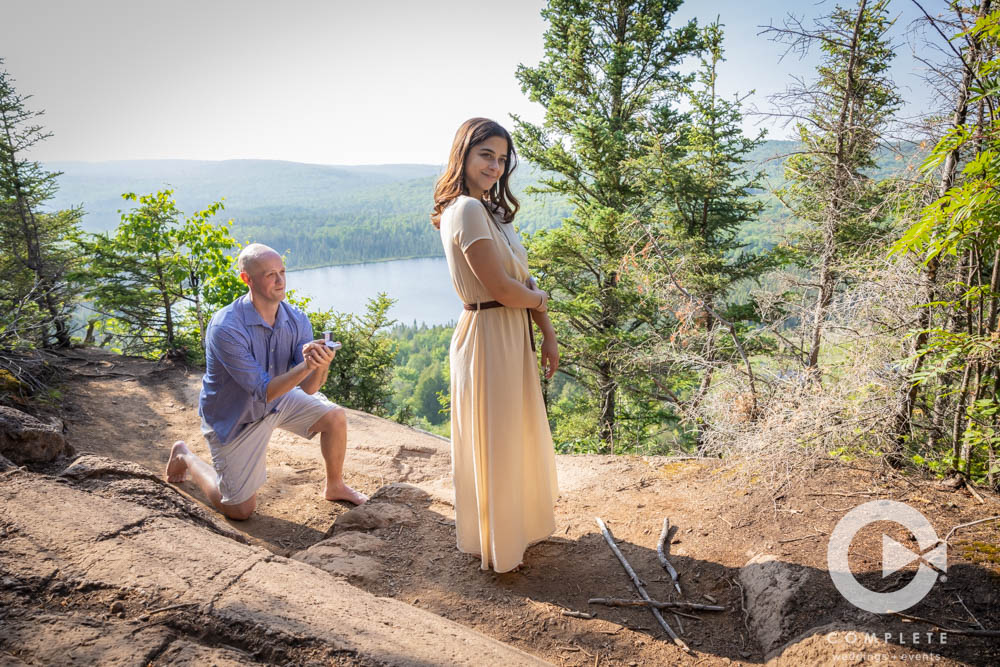 Adam kneeling behind Nicole before she turns for the Suprise proposal