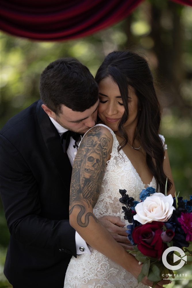 Groom kissing bride shoulder who is holding flowers