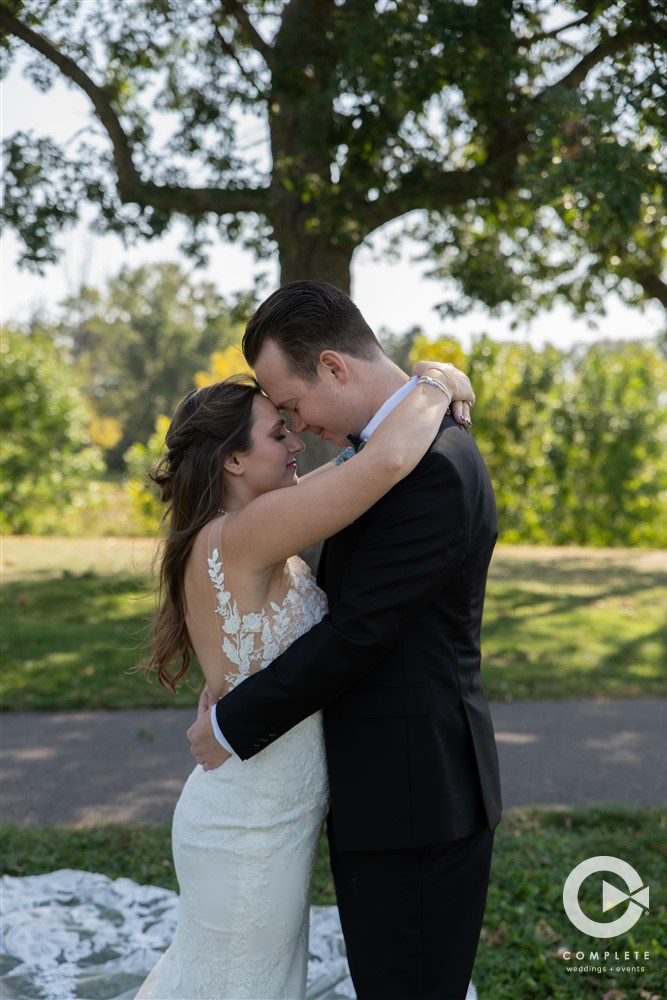 Bride and Groom embrace in front of tree captured by Complete Weddings and Events