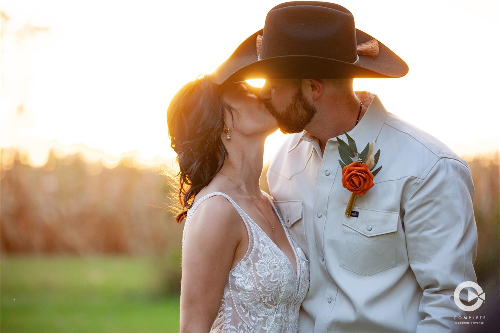 Bride and Groom kissing during golden hour with sun behind them while they kiss, photo by Complete Weddings + Events