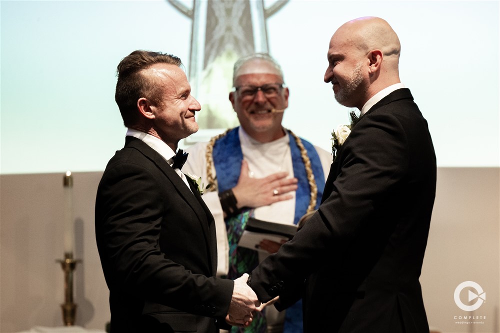 Groom and Groom looking into each others eyes and smiling with minister in background