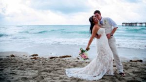 bride and groom kissing, on the beach, on the sand with the pier in the background