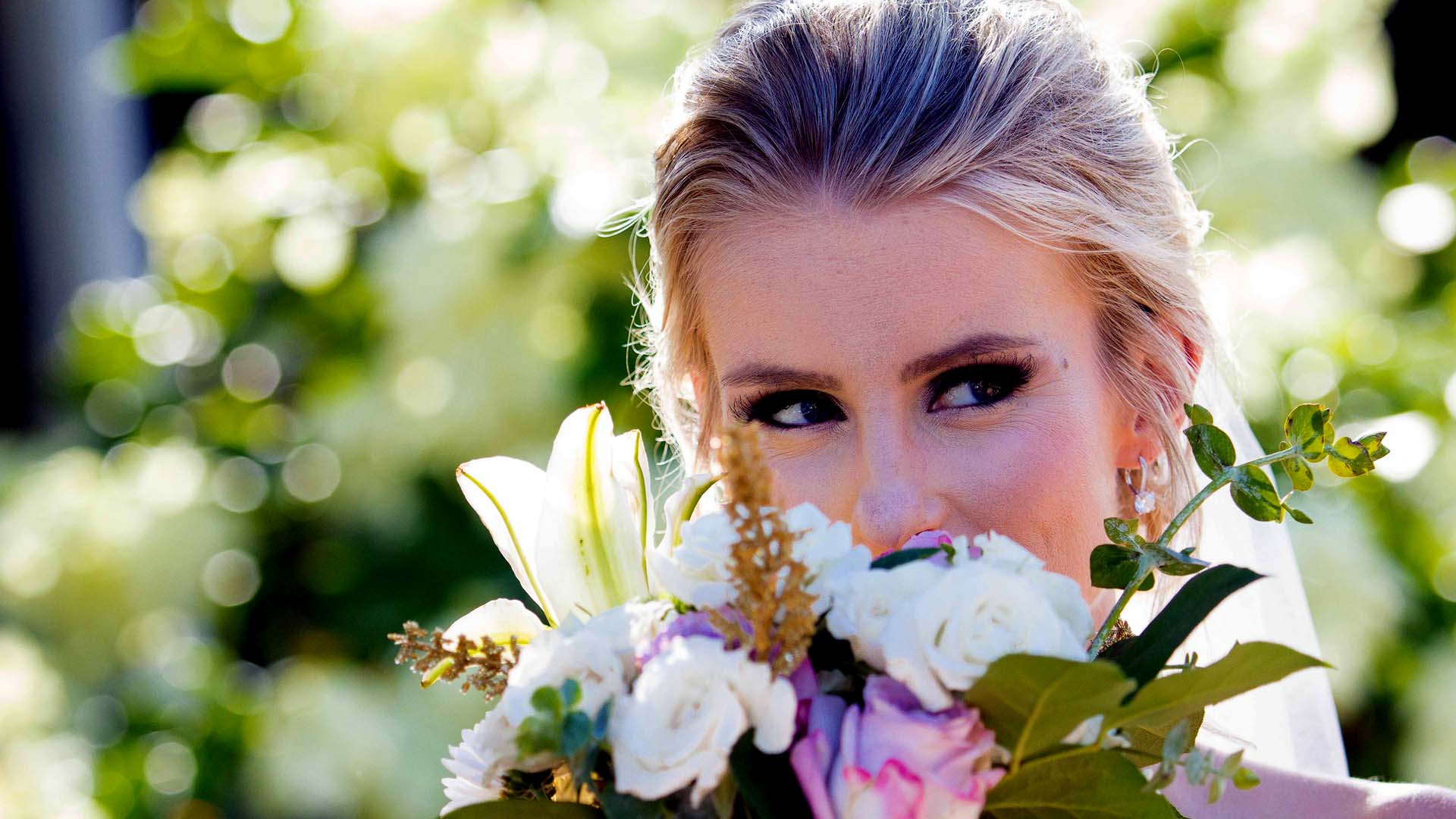 Bride holding bouquet of flowers close to her face so you just see her eyes