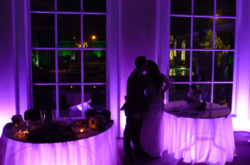 bride and groom kissing with purple lighting under sweetheart table and cake table
