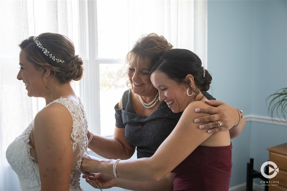 mom and sister helping bride into her dress