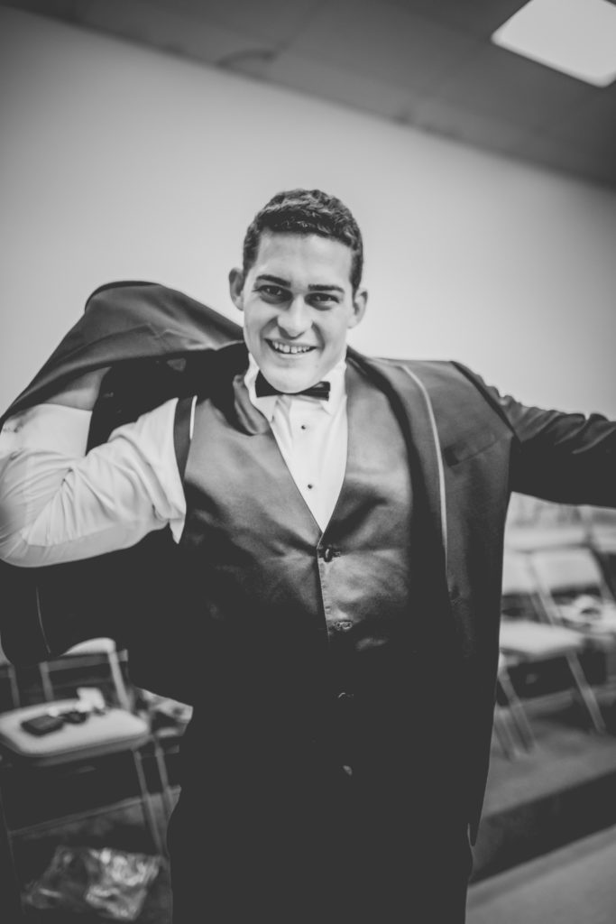 Black and white photo of Kansas City groom putting on his tuxedo coat.