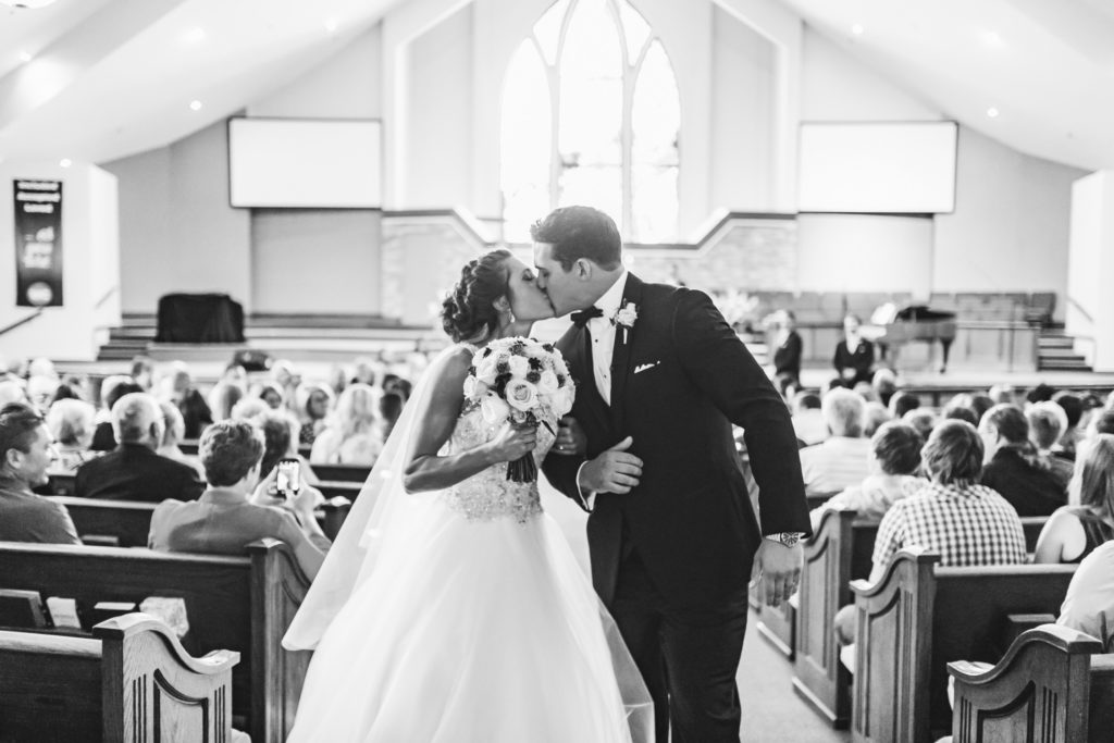 Black and white photo of bride and groom kissing as they exit the ceremony at Woods Chapel United Methodist Church in Lee's Summit.