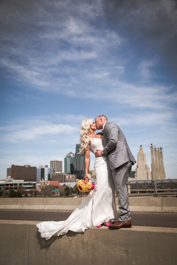 Bride and groom share a kiss on a bridge with the Kansas City skyline in the background