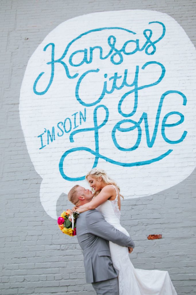 Groom holds bride up in the air in front of iconic mural in Kansas City