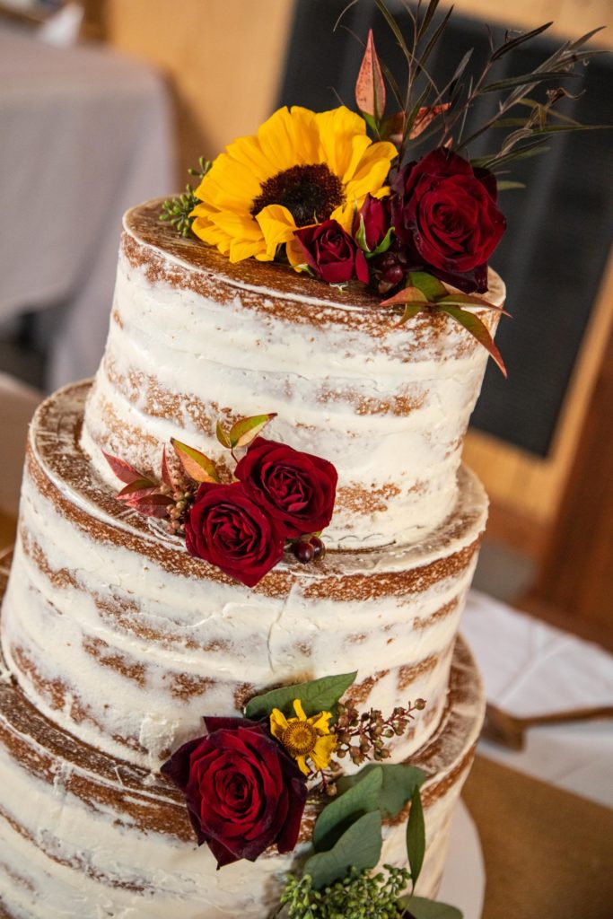 Photo of tiered-cake adorned with sunflowers and red roses at a Kansas City wedding.