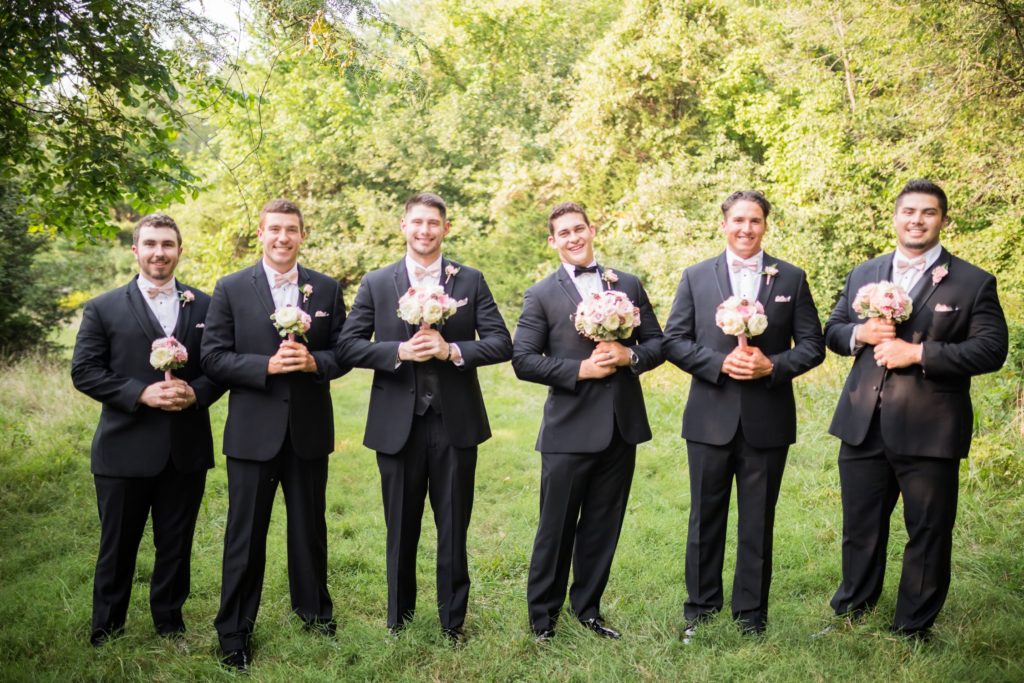 Fun photo of groomsmen holding the bridesmaids' pink and white rose bouquets..