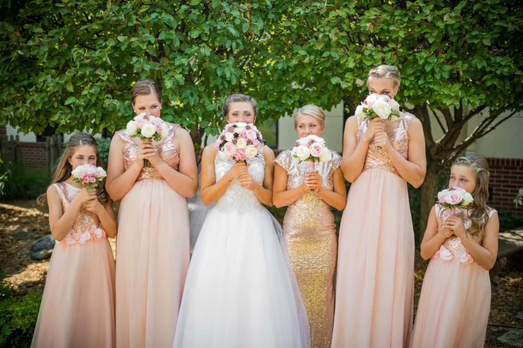 Bride and bridesmaids holding white and pink rose bouquets in front of their faces.