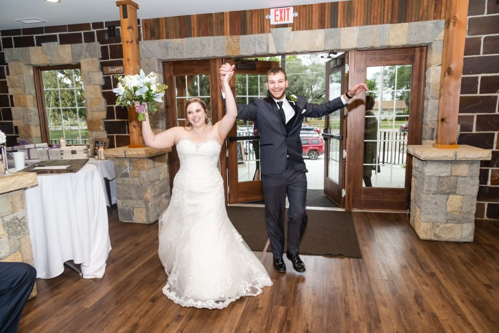 Bride and groom entering there reception, smiling, hands raised.