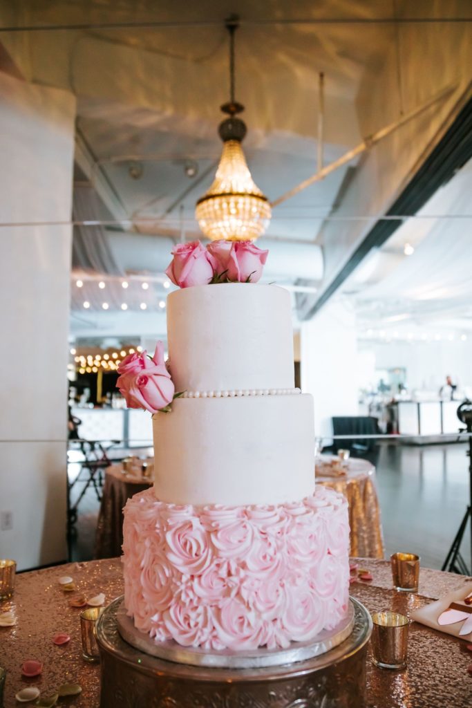Close up of a three tier cake, the two top tiers are white while the third layer is covered in pink roses
