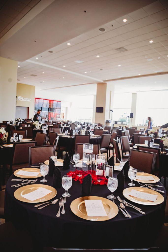 Arrowhead Stadium set up for a wedding reception. The tables have black tablecloths with gold plates and red centerpieces