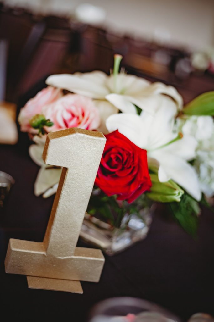 Close up of centerpieces featuring a golden table number with roses and lilies