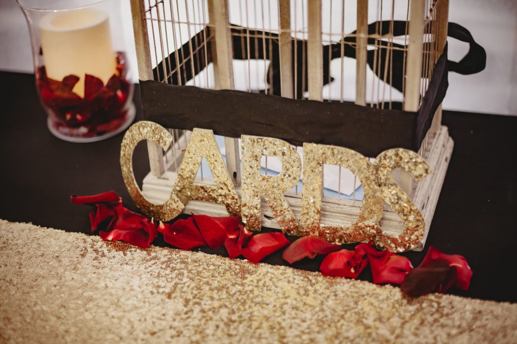 Card basket at a wedding reception decorated with gold glitter and red rose petals