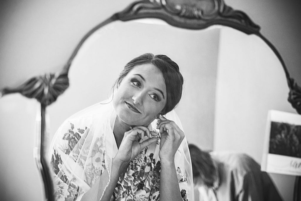 Bride looks in antique mirror to put earrings on