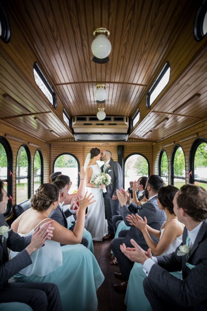 Bride and groom share a kiss on a trolly in Kansas City while the bridal party cheers