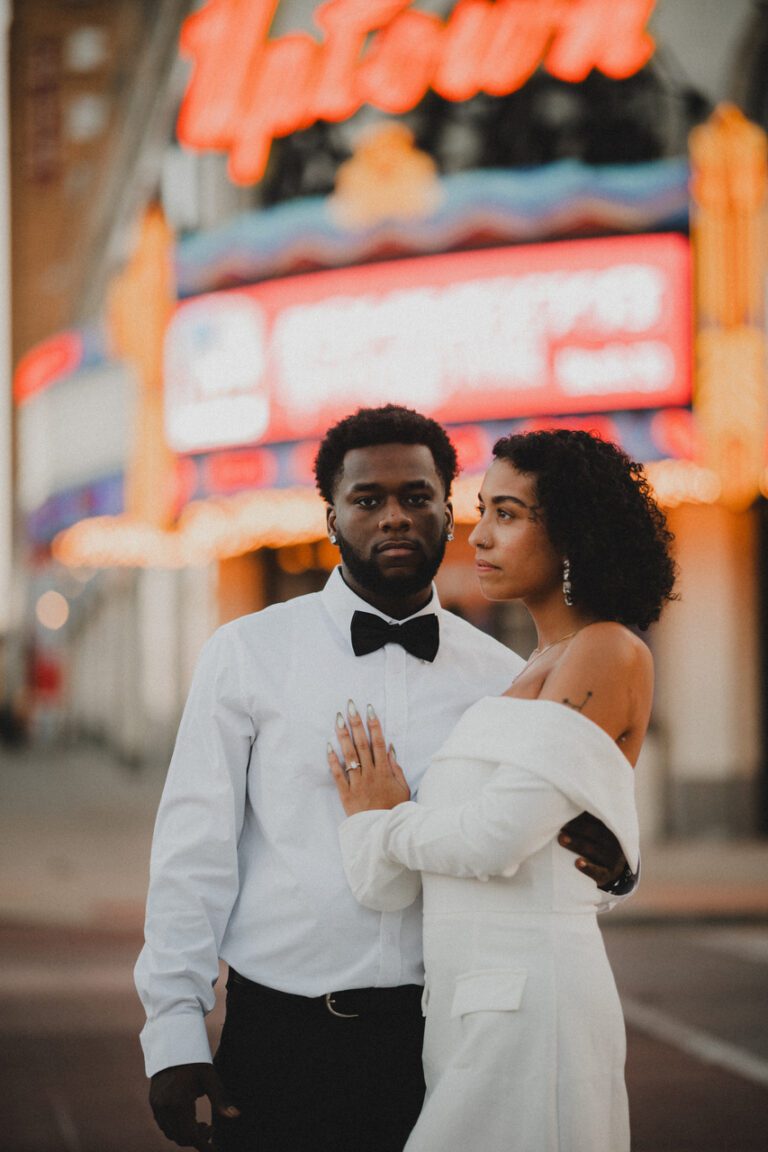 Engaged couple standing close together in front of the bright Uptown Theater marquee in Kansas City during their engagement photos photographed by Gabriel with Complete Weddings and Events