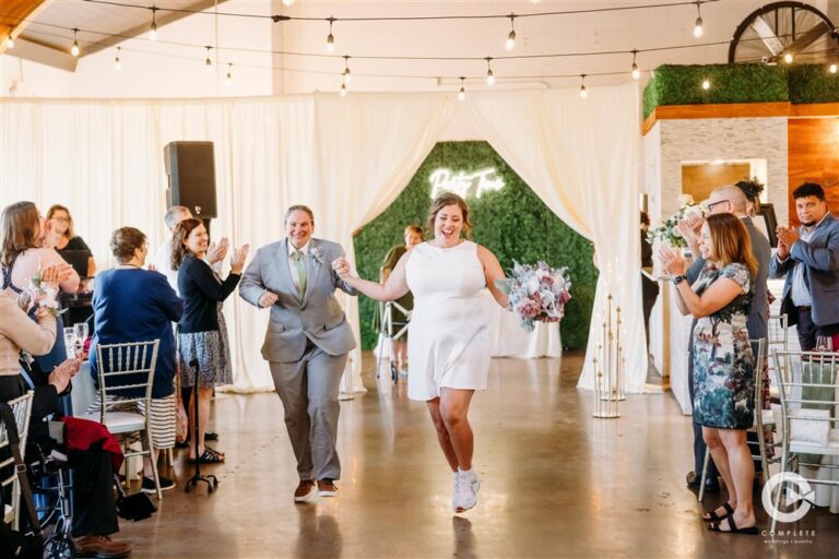 Newlywed couple running into their wedding reception holding hands at The Martin Event Space while guests cheer photographed by Kansas City wedding photographer Gabriel