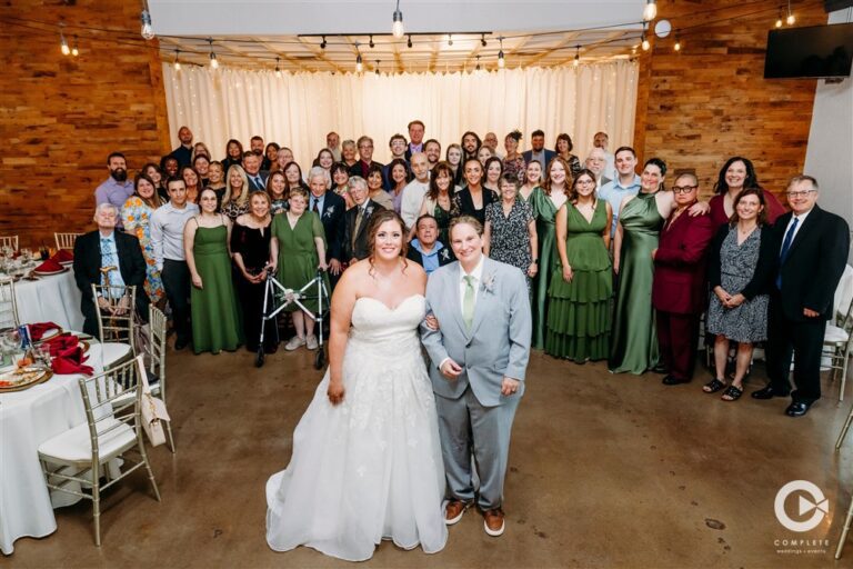 Wedding couple standing in front of all their guests for a large group photo inside The Martin Event Space reception hall photographed by Kansas City wedding photographer Gabriel