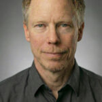 Headshot of Josh, a videographer for Complete Weddings and Events, wearing a dark shirt against a gray studio background.