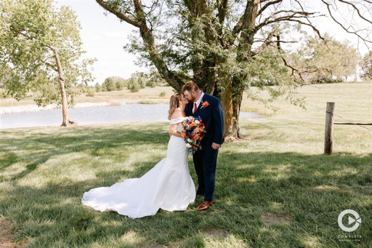 Bride and groom standing together with colorful bouquet by the pond at Tobacco Barn Farm wedding venue near Kansas City photographed by Complete Weddings and Events photographer Kim Miller