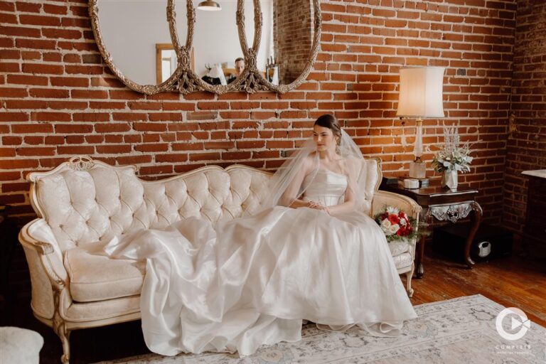 Bride in satin wedding dress sitting on vintage sofa in the lounge at The Oliver Building wedding venue photographed by Complete Weddings and Events photographer Kim Miller