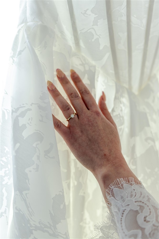 Close-up of the bride's hand and gold engagement ring against her lace wedding gown at Cedar Valley Forest in De Soto, Kansas