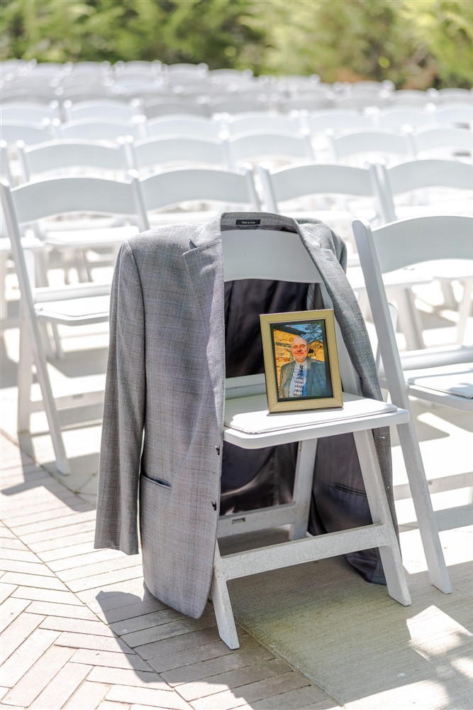 Memorial tribute with a gray suit jacket draped over a white ceremony chair holding a framed photo of a loved one at Cedar Valley Forest in De Soto, Kansas