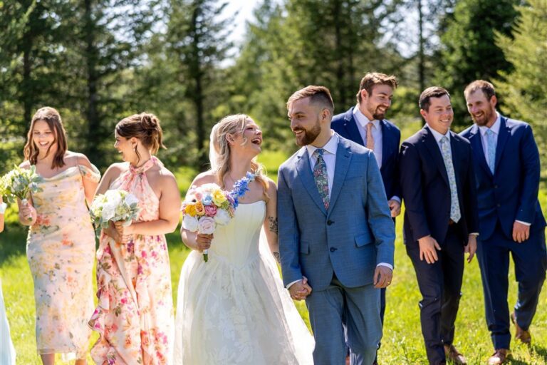 Bride and groom laughing while walking through a sunny green field with their wedding party at Cedar Valley Forest in De Soto, Kansas