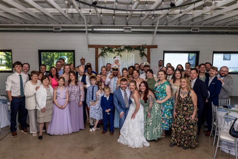 Large group photo of the bride, groom, wedding party, and all guests inside the white barn reception hall at Cedar Valley Forest in De Soto, Kansas