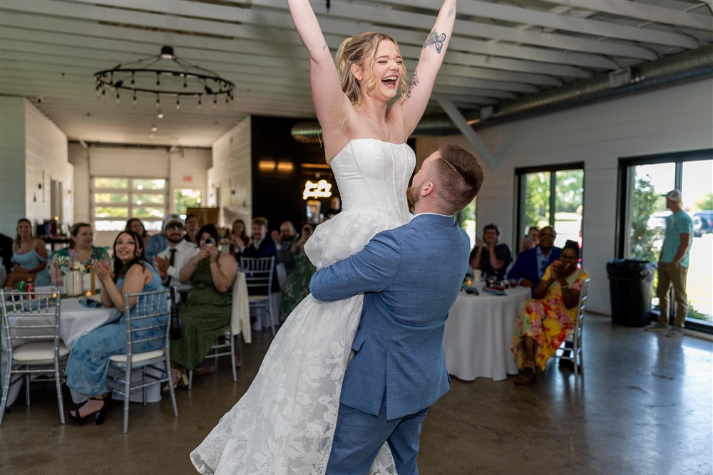 Groom lifting the laughing bride into the air with her arms raised in celebration during the reception at Cedar Valley Forest in De Soto, Kansas