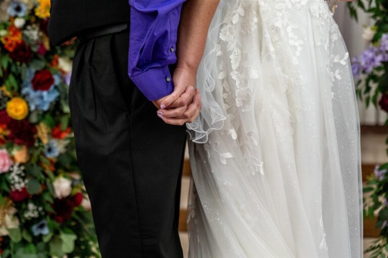 Close up of a bride and groom holding hands at the altar, showing sparkle tulle and lace gown detail and a purple dress shirt, at a Richmond, Missouri church wedding