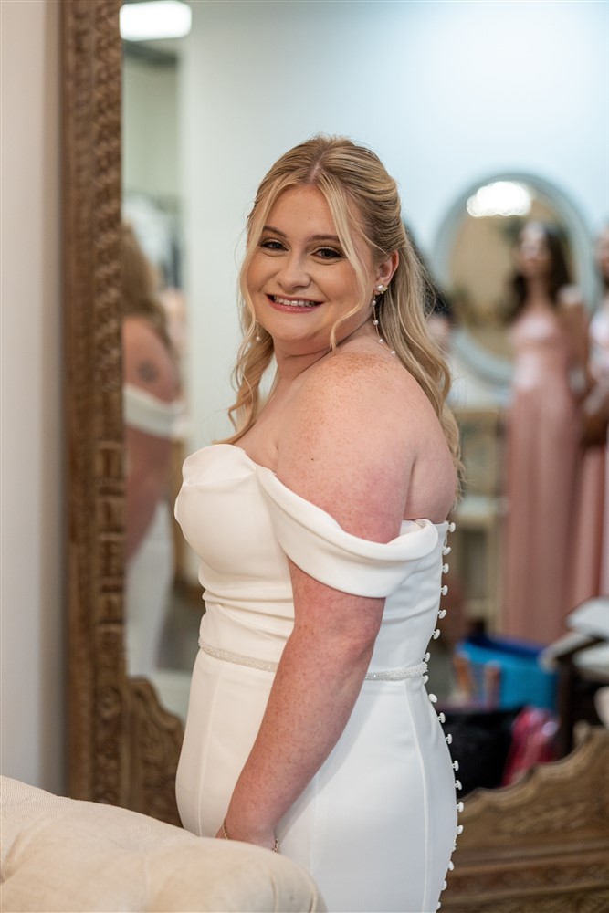 Bride looks over her shoulder beside an ornate wood mirror in the bridal suite at The Stanley