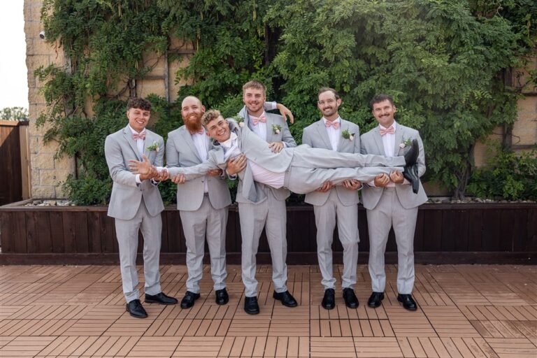 Five groomsmen in grey suits hold the groom horizontally while laughing on the patio at The Stanley