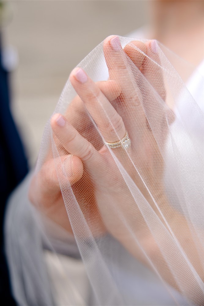 Close-up of a bride's hands and diamond engagement ring resting on the tulle of her wedding veil